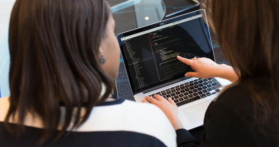two women looking at the code at laptop
